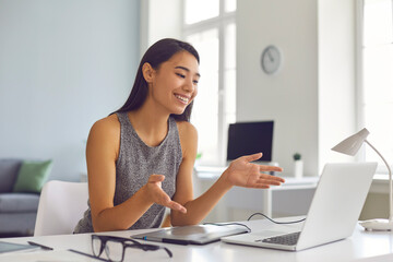 Happy young Asian woman sitting at desk at home and using laptop computer for video call