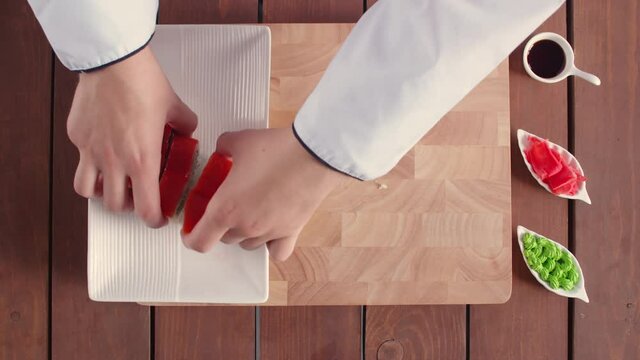 Traditional japanese food. On a white rectangular platter, the man beautifully puts six Philadelphia rolls, and also puts cups with ginger, soy sauce and wasabi. The dish stands on one half of a