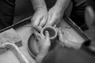 Close-up of men's and children's hands on a potter's wheel. Pottery training. Black and white photo.