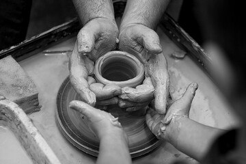 Close-up of men's and children's hands on a potter's wheel. Pottery training. Black and white photo.