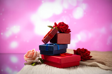 Boxes with gifts lie on the table next to roses against a pink bokeh background. Gifts for the holiday. Valentine's Day gifts. International Women's Day. Love.