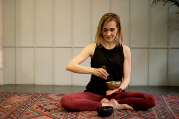 Woman playing on Tibetan singing bowl while sitting on yoga mat. Vintage tonned.