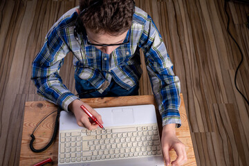 Boy with shirt and glasses makes notes on laptop with fountain pen