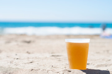 Plastic glass with cold beer on the beach sand