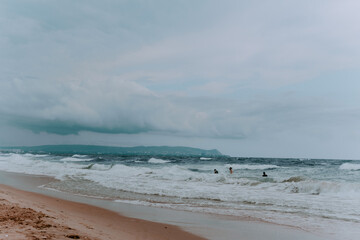 a few people are swimming in the sea in a storm. stormy skies and huge waves of the sea. sandy beach. seagull in the sky