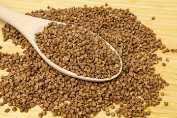 Buckwheat groats scattered on wooden bamboo table with spoon.