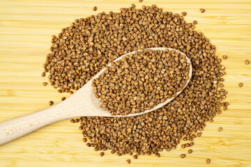 Heap of buckwheat groats with a spoon on wooden table, top view.