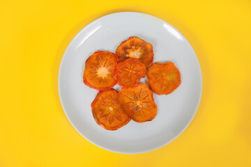 Persimmon chips lie on a porcelain plate on a yellow background.