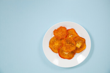 Persimmon chips lie on a porcelain plate on a blue background. View from above. Flat lay.