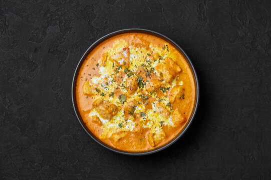 Murgh Makhani or Butter Chicken in black bowl on dark slate table top. Indian Cuisine dish with chicken meat and creamy masala. Asian food and meal. Top view