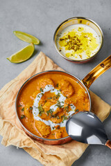 Murgh Makhani or Butter Chicken in copper bowl on gray concrete table top. Indian Cuisine dish with chicken meat and creamy masala. Asian food and meal.