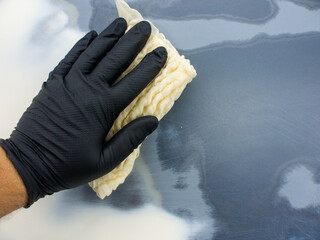 the hand of the auto painter in a black glove holds a special napkin for dusting the surface of the car.