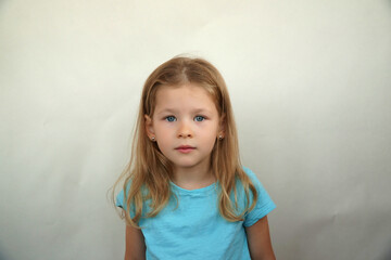 Naklejka premium Cute little girl shows emotions on a white background in a T-shirt. Simple beauty. High quality photo