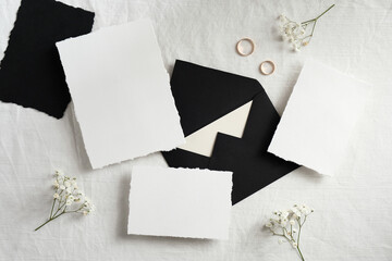 Wedding stationery mockup top view. Blank greeting cards, black envelopes, golden rings, flowers on whit bed. Wedding cards design.