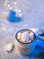 Obraz na płótnie Canvas a white cup with a knitted scarf, hot cocoa or chocolate with marshmallows and cinnamon . festive home atmosphere of comfort