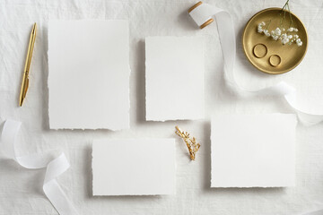 Empty white wedding stationery mockups with golden rings, pen, ribbons on white bed. Flat lay, top...