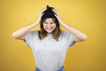 Beautiful young caucasian girl wearing french look with beret over isolated yellow background suffering from headache desperate and stressed because pain and migraine with her hands on head