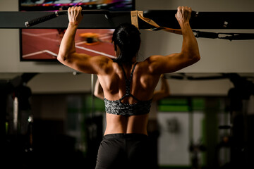 Fototapeta na wymiar Close-up view of muscular woman doing pull ups in gym. Bodybuilding concept.