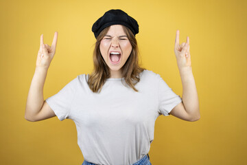 Beautiful young caucasian girl wearing french look with beret over isolated yellow background shouting with crazy expression doing rock symbol with hands up