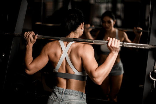 close-up view of adult brunette woman doing exercise with barbell in gym.