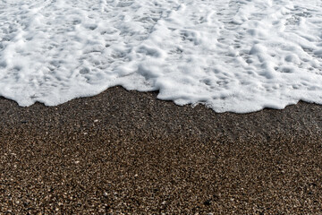 White sea foam on multi-colored pebbles. Close up.