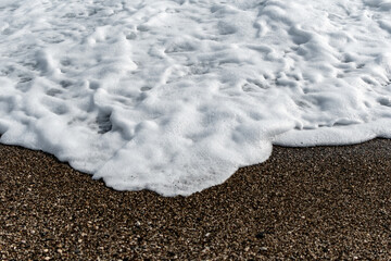 White sea foam on multi-colored pebbles. Close up.