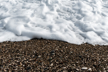 White sea foam on multi-colored pebbles. Close up.