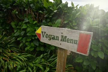 vintage old wooden signboard with text vegan menu near the green plants.