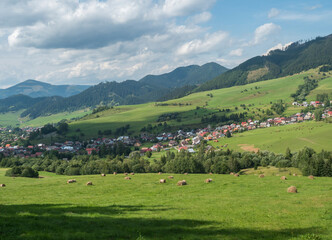 Fototapeta na wymiar view on village Liptovska Luzna at the foothills of Low Tatras mountains with lush green meadow, forested hills and straw bales. Slovakia, summer sunny day, blue sky white clouds background