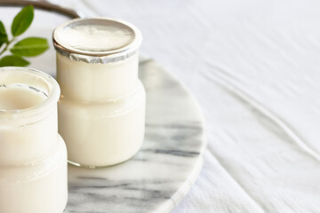 Two portions of fresh natural organic yogurt in a glass jars on marble tray. Homemade greek yogurt with wooden spoons. Healthy breakfast. Top view.