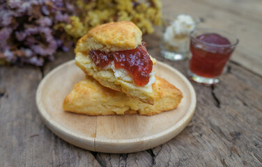 Scones with Strawberry Jam and Clotted cream in a wooden plate on a wood table. Flower background
