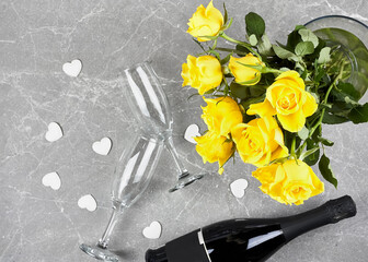 Yellow roses, bottel of sparkling wine, champagne flute and white hearts on gray background.Gift,holiday,Dating. Valentines day,Mothers day,Womens day