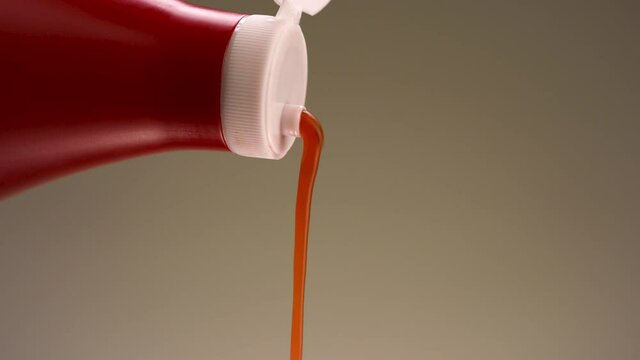 Adding tomato sauce from a plastic bottle of red color. Stock footage. Pouring natural ketchup isolated on beige wall background. 