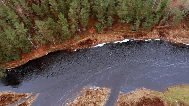 Red sandstone cliffs in the banks of river Salaca during late autumn time, Latvia. Real time drone footage