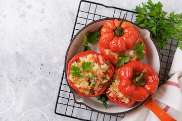 Red bell peppers stuffed with rice and vegetables on cast iron pan on gray concret background.