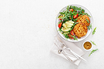 Grilled chicken burgers, avocado and fresh vegetable salad with tomato and arugula, top view