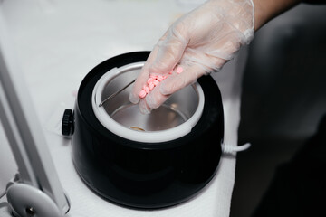 Close-up view of female hand in a glove with pink wax before melting. Depilation concept, waxing, smooth skin without hair. Beauty salon device for heating wax. Preparation for the cosmetic procedure