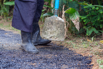 Man holding a cement rod for hammering to adjust the asphalt surface for the walkway. Close-up photo. Constructed from asphalt. Space for text