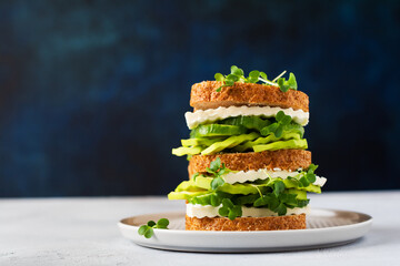 Avocado, cucumber and feta cheese sandwich decorated with micro-greens and multi-grain bread on a simple wooden stand for a healthy breakfast. Selective focus.