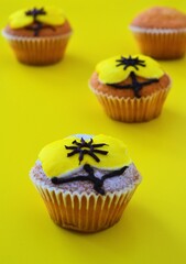 Rows of muffins decorated with powdered sugar and yellow flower shaped icing on a yellow background