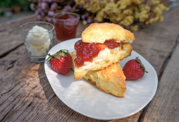 Selective focus Scones with Clotted cream and Strawberry Jam  in a wooden plate on a wood table. 