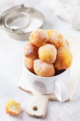 Little Donuts. Home-made cottage cheese cookies deep-fried and sprinkled with icing sugar in a vintage ceramic cup on a light background. Selective focus.