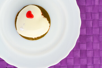 A cake in heart shape. One heart-shaped mousse cupcake on a plate on a purple background. Valentine's Day.