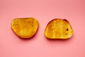 two slices of toasted bread lie on a pink background