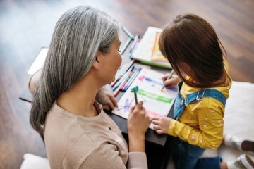 Grandmother sitting beside granddaughter during drawing