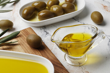Composition of green olives in oil, olive branch, gravy boat on a marble background. Space for text.