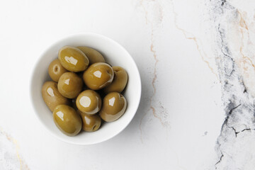 A bowl of green olives on a marble table, space for text.