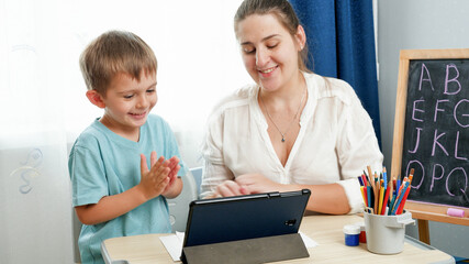 Smiling happy boy studying and learning on tablet computer with young smiling mother. Home...