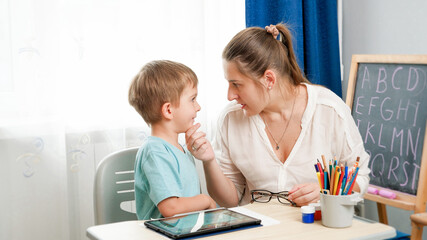 Angry mother looking and talking to her silly little son doing homework at home. Conflict between parent and child.