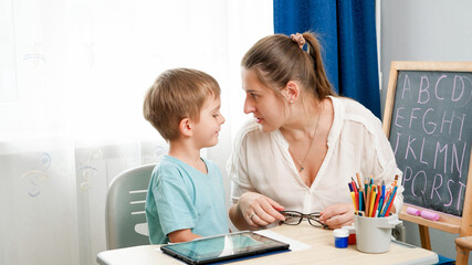 ANgry mother looking in face of her little son being silly while doinghomework at remote home school lesson